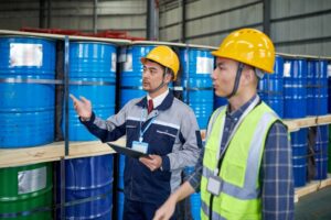 Two asian male worker examining & discussing in chemicals buckets warehouse. Report, track, and prevent unsafe workplace condition right from Q-Hazard Reporting App