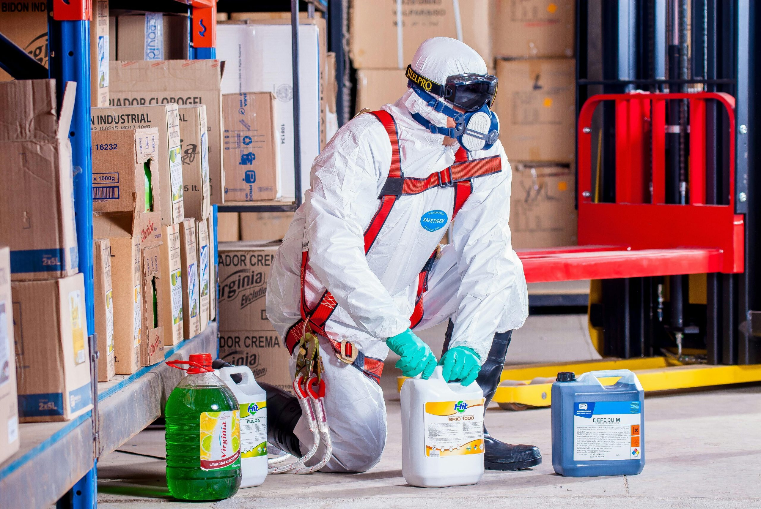 Worker in white hazmat suit handling chemical containers in a warehouse setting