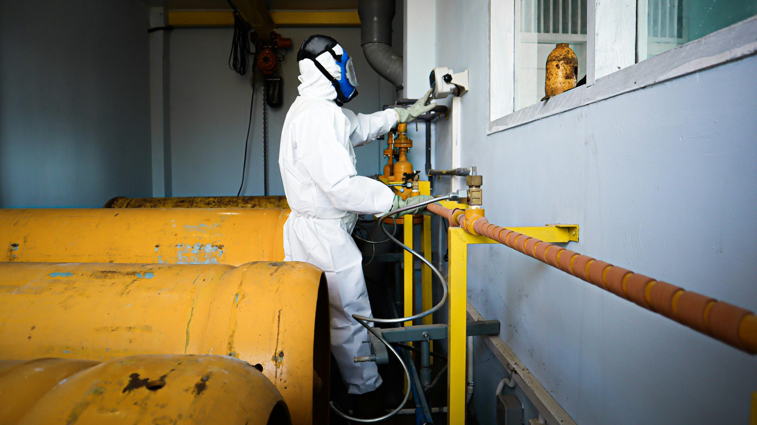 Industrial worker in full protective suit and gas mask handling chemical pipes in a facility
