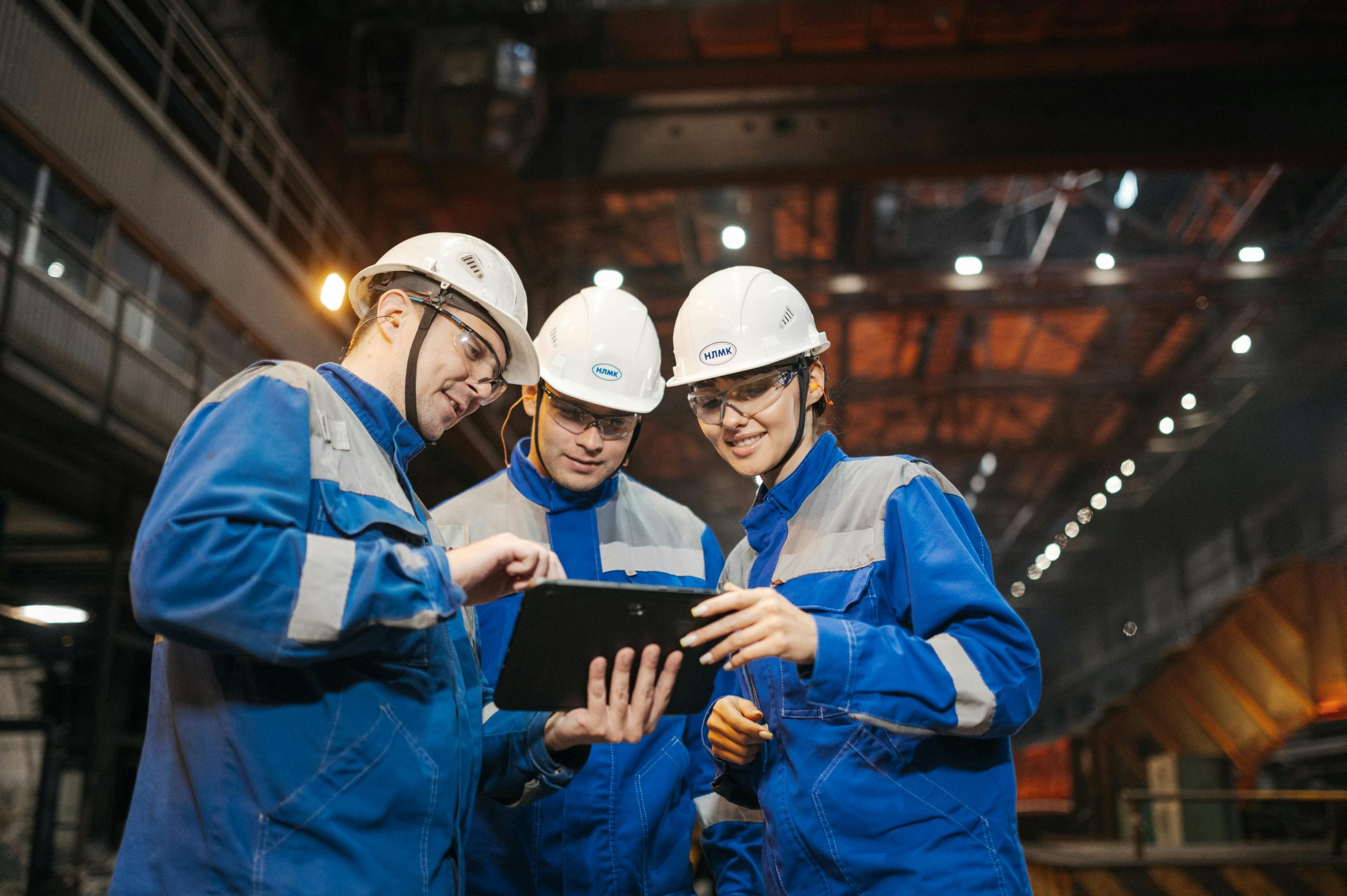 Two EHS engineers in hard hats reviewing near-miss data on a tablet in an industrial facility