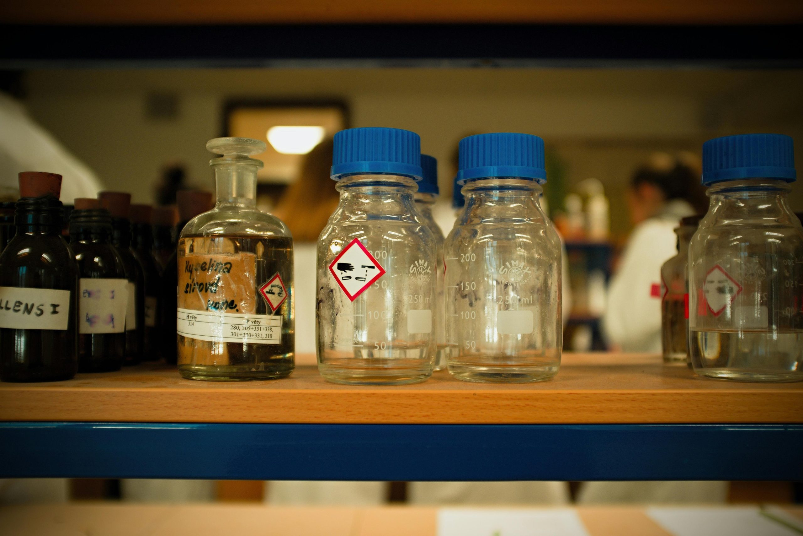 Glass chemical bottles with GHS hazard warning labels on a laboratory shelf