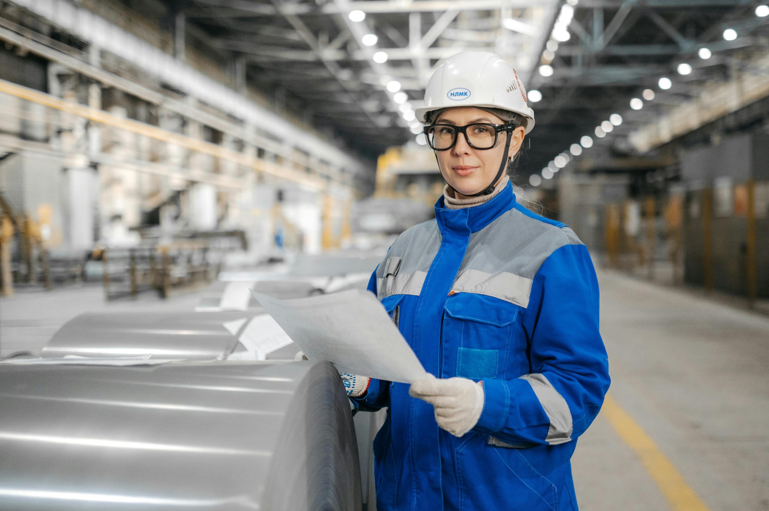 Female engineer in blue work gear and hard hat reviewing documents in an industrial plant