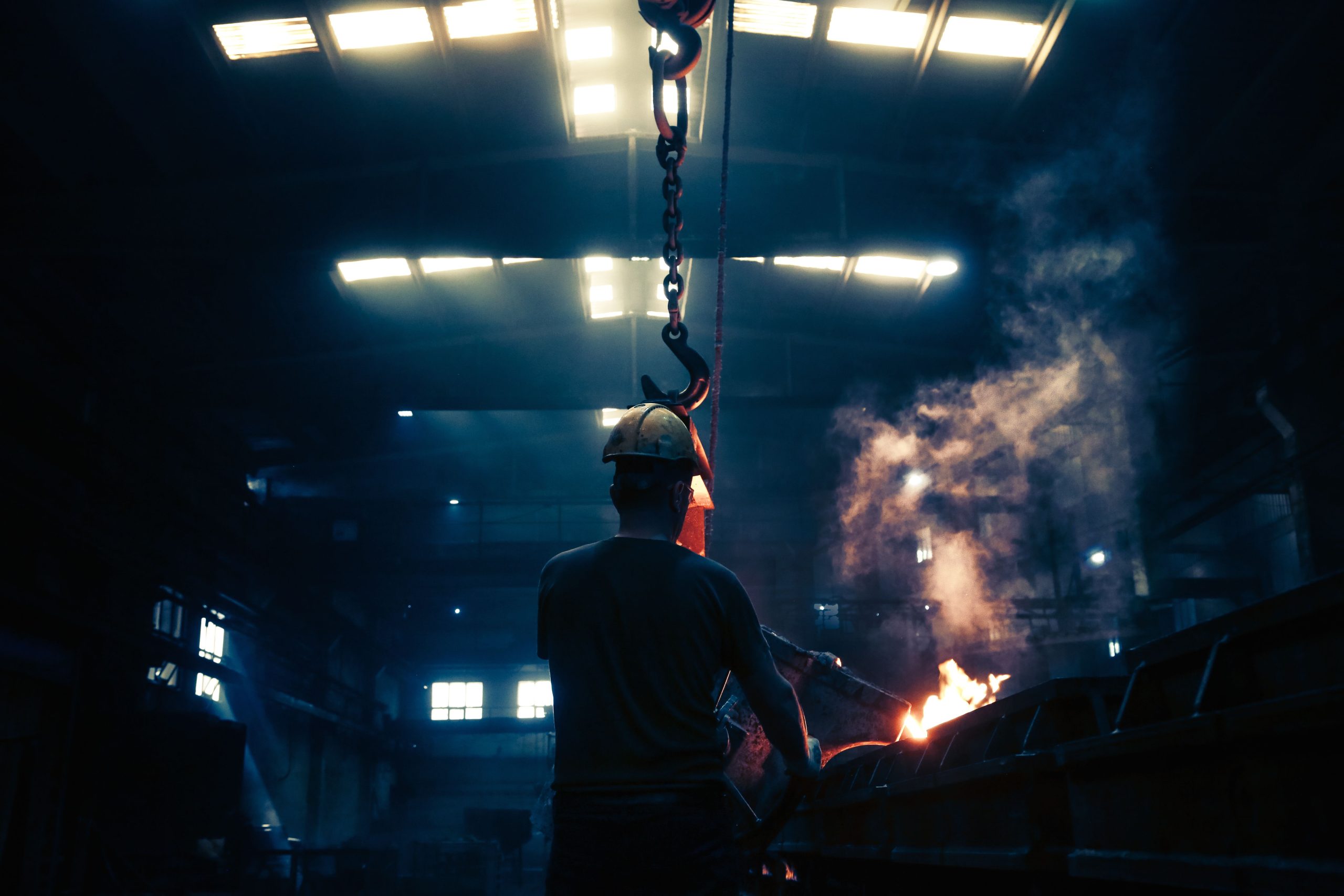 Industrial worker wearing hard hat in a hot factory environment with visible heat and fire