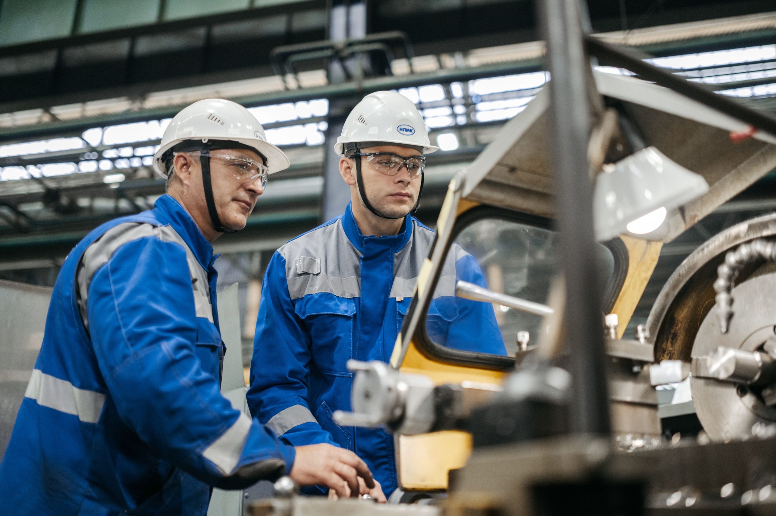 Two industrial workers in PPE operating machinery together on a factory floor