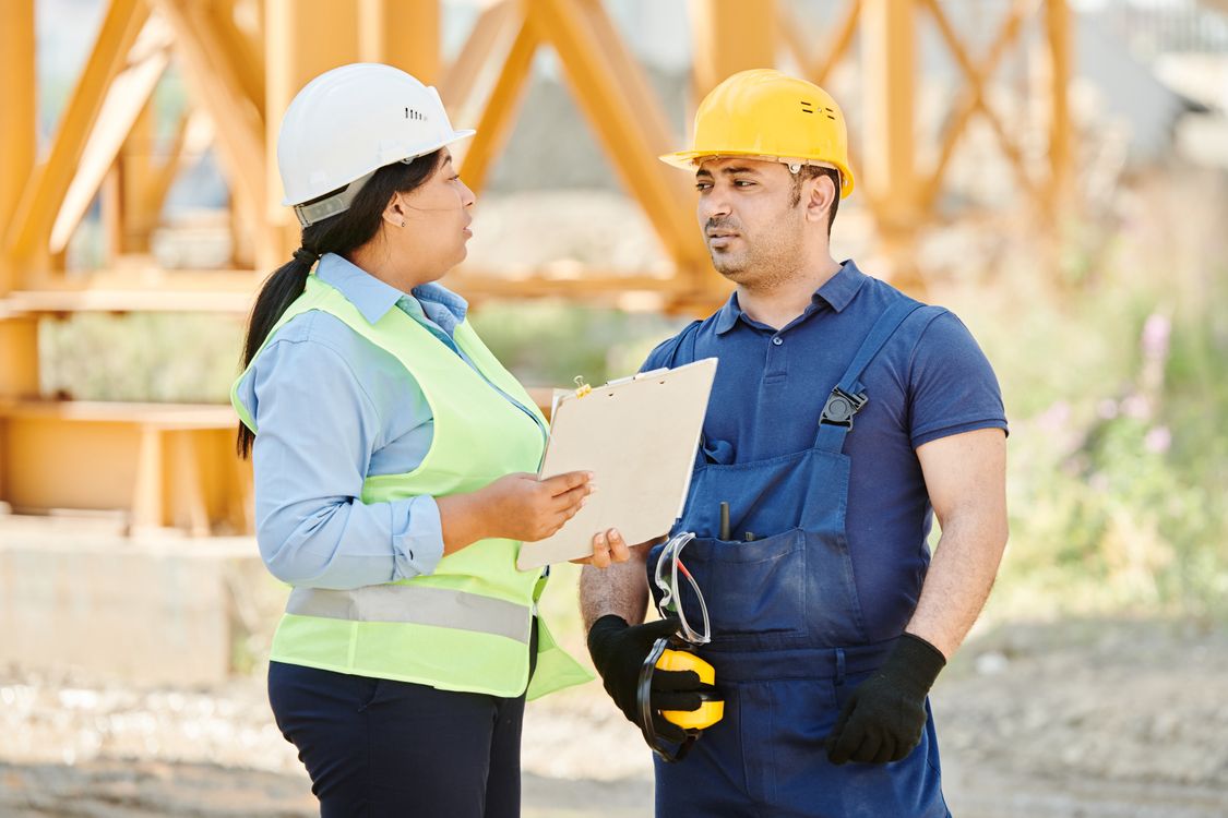 Two workers in hard hats and safety vests discussing safety on a construction site