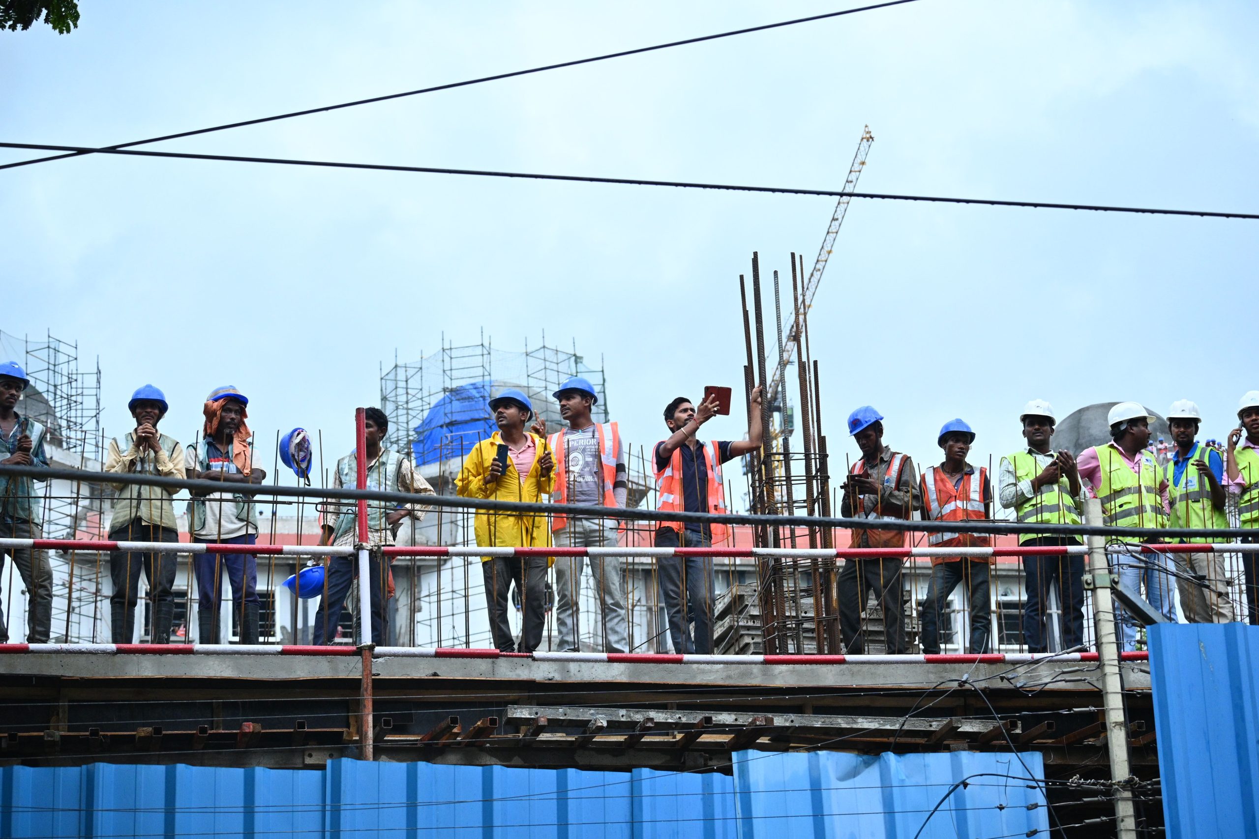 Group of contractor workers in hard hats and safety harnesses standing on scaffolding at a worksite