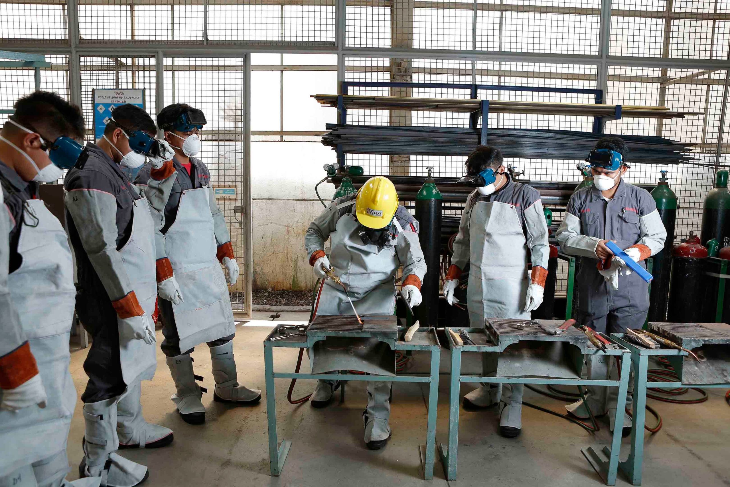 Workers in white protective suits and helmets during an industrial welding and safety training exercise