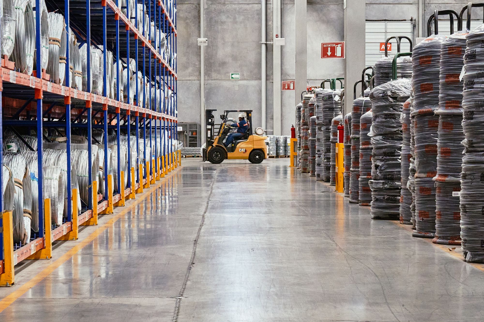 A forklift moving a load down an aisle of pallet racking in an industrial warehouse