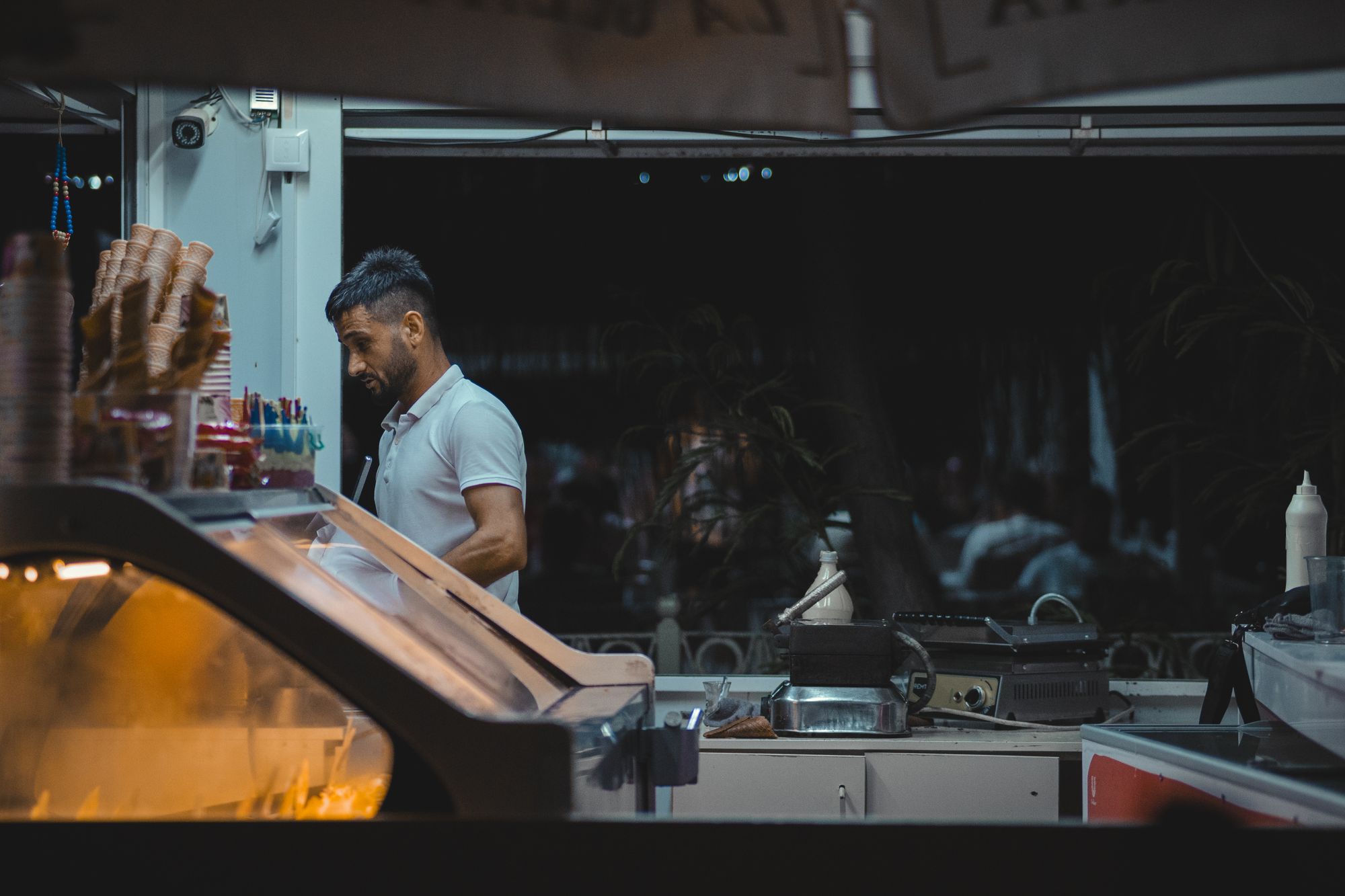 A single worker standing behind a dimly lit service counter at night with no one else nearby