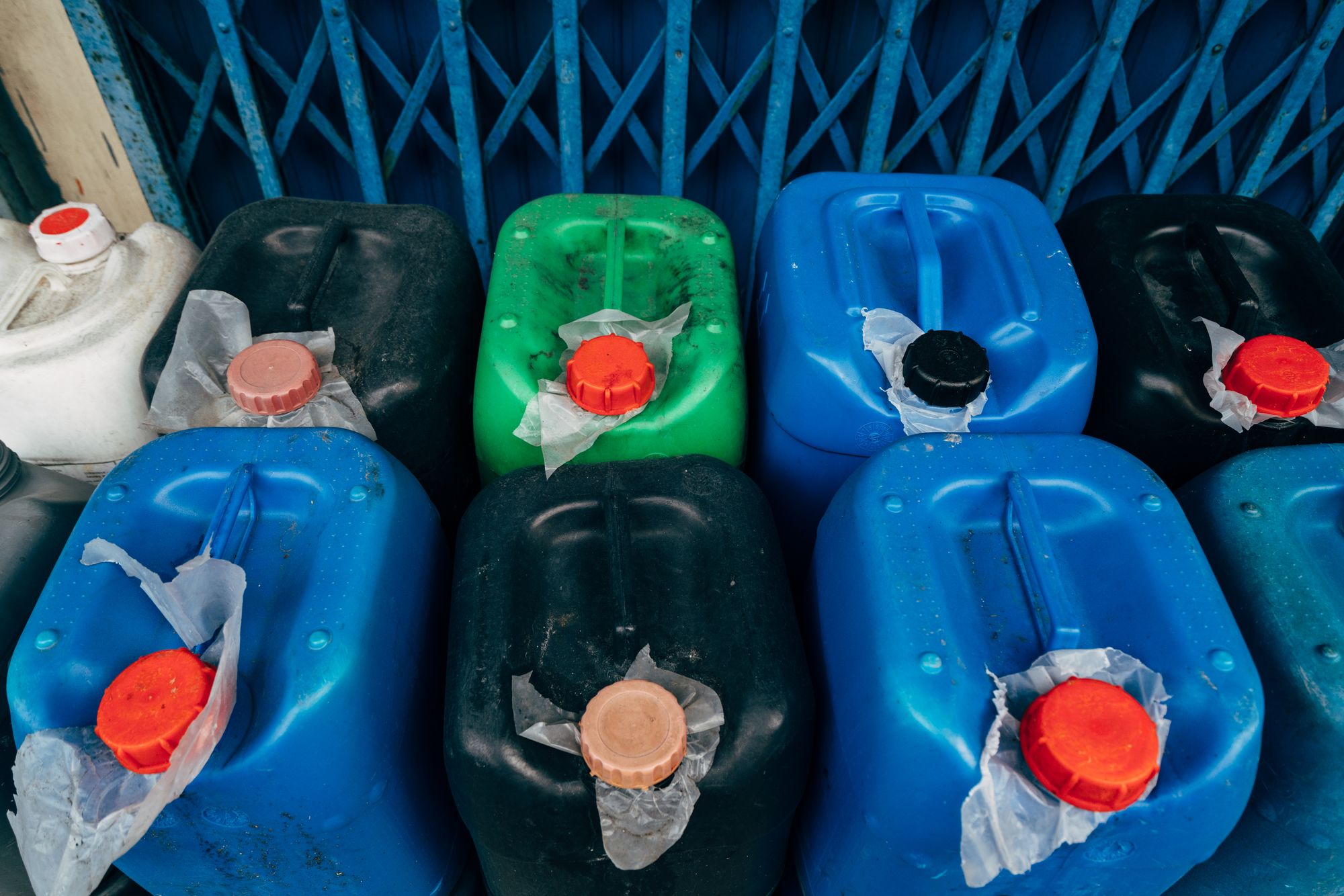 A row of stacked plastic jerrycans holding chemicals, none of them carrying a workplace label