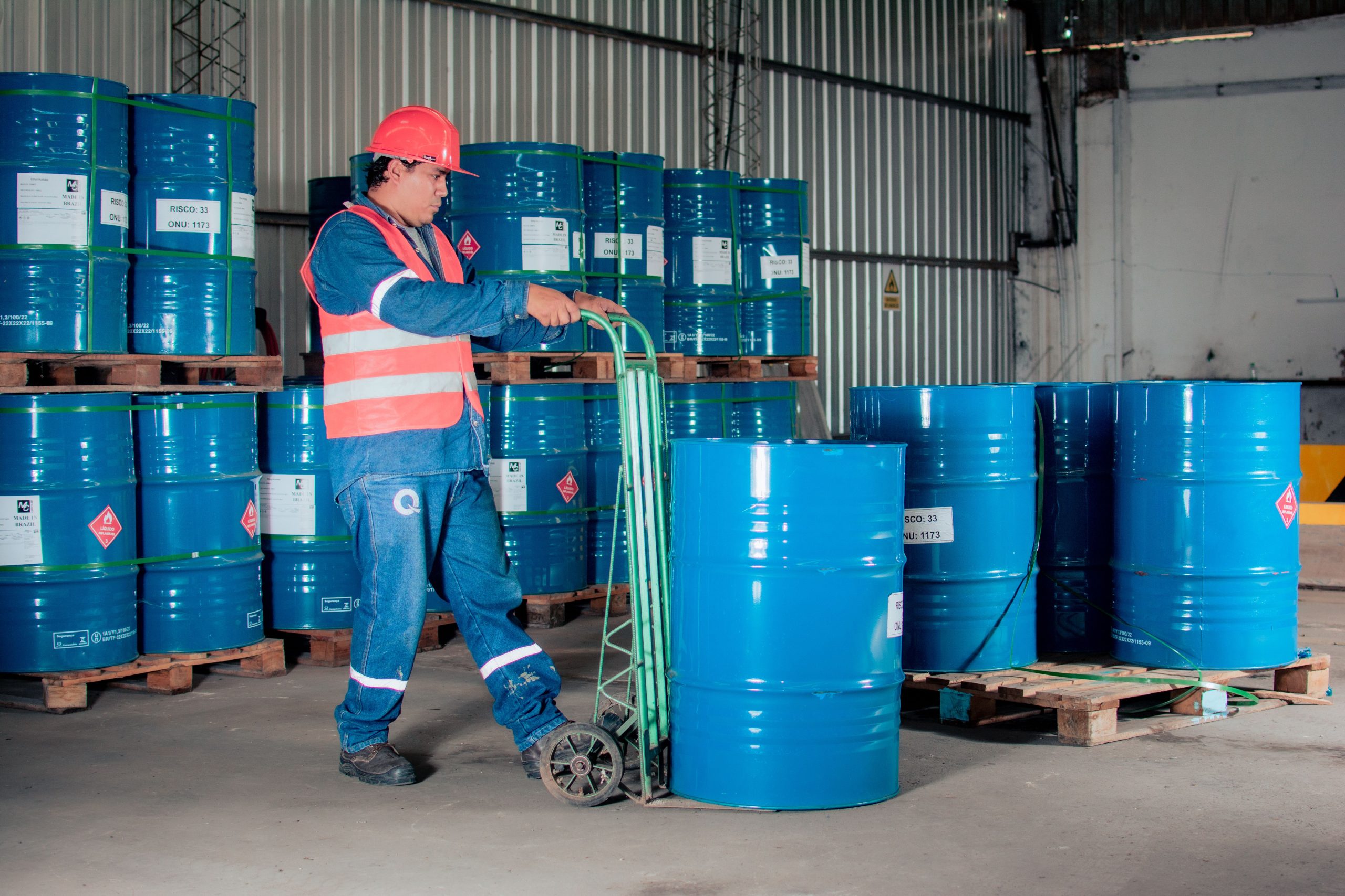 Industrial worker using a hand truck to move blue chemical drums in a warehouse receiving area