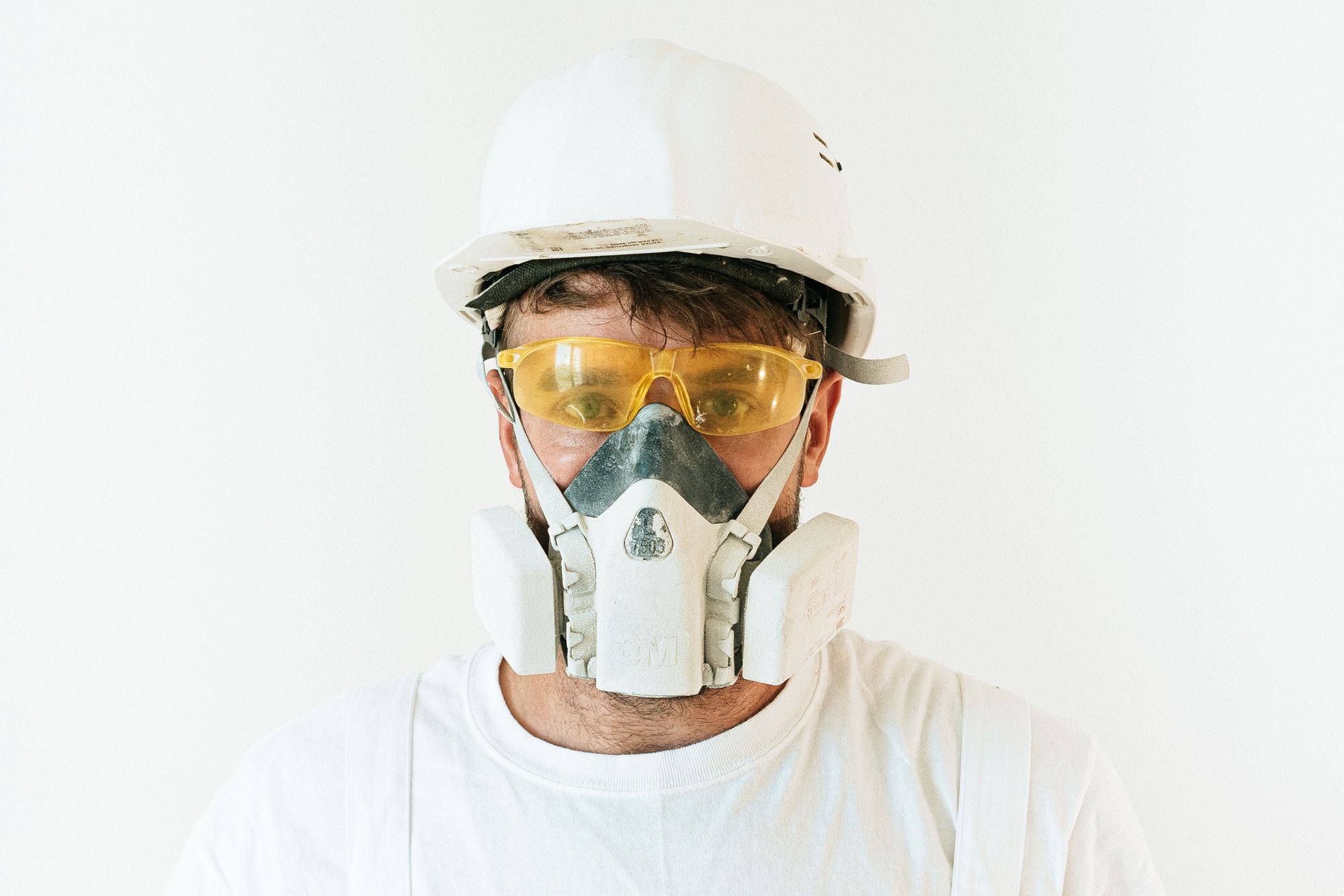 Industrial worker wearing a tight-fitting half-mask respirator, safety glasses and a white hard hat