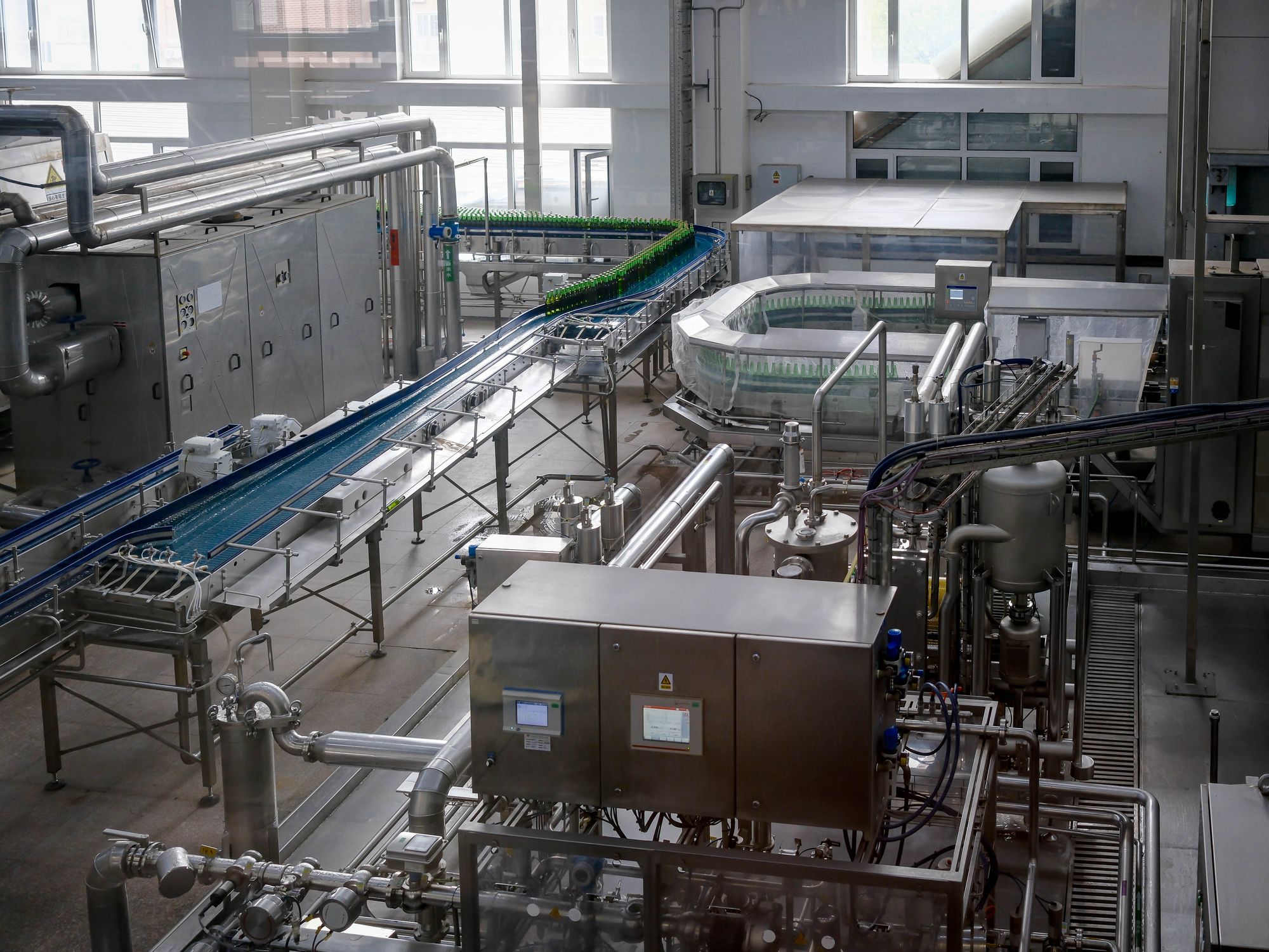 Overhead view of a beverage bottling plant with conveyors, filling equipment and control panels, the kind of machinery a job hazard analysis breaks into steps