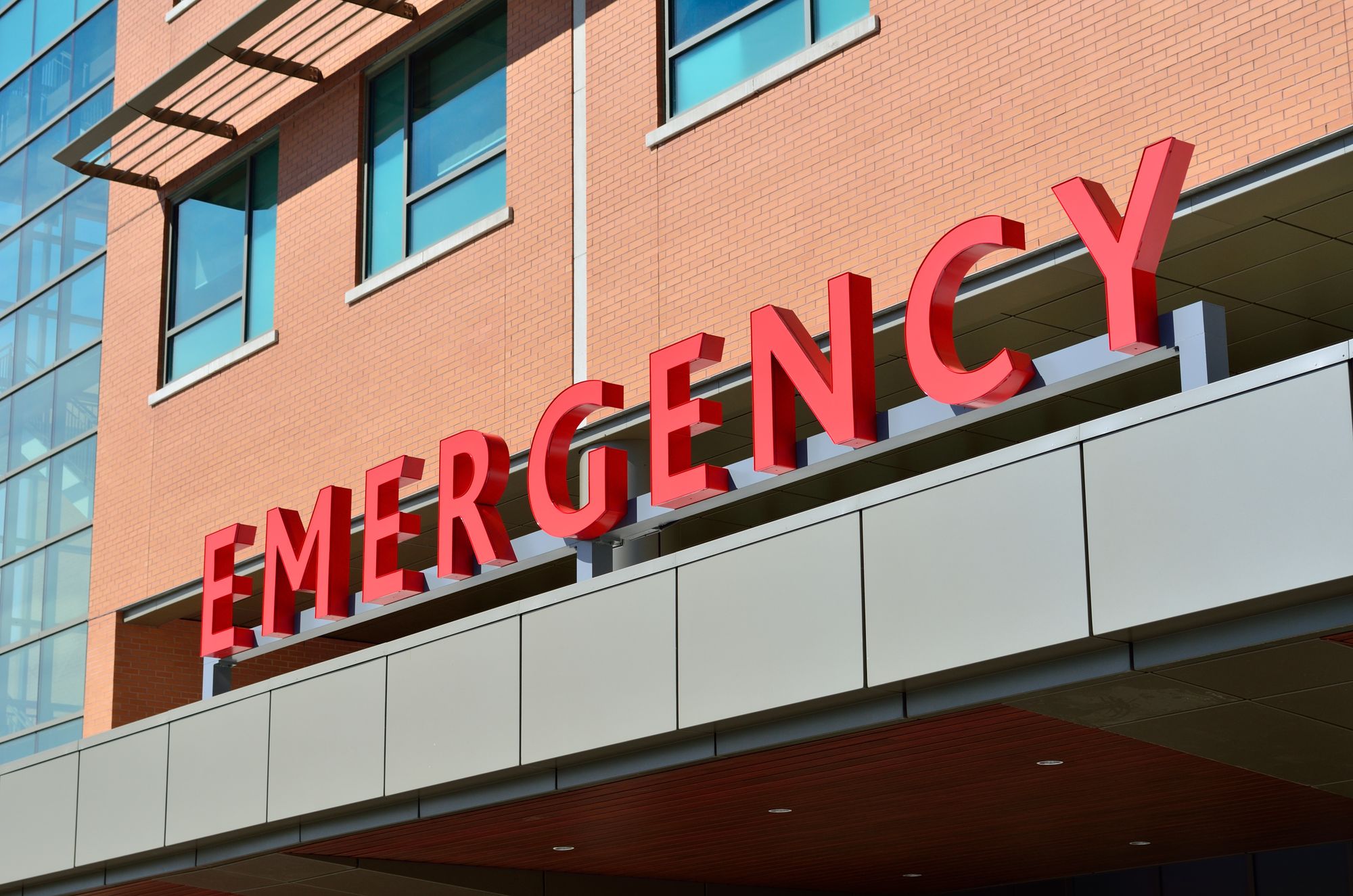 Red EMERGENCY letters mounted on the canopy above a hospital emergency department entrance