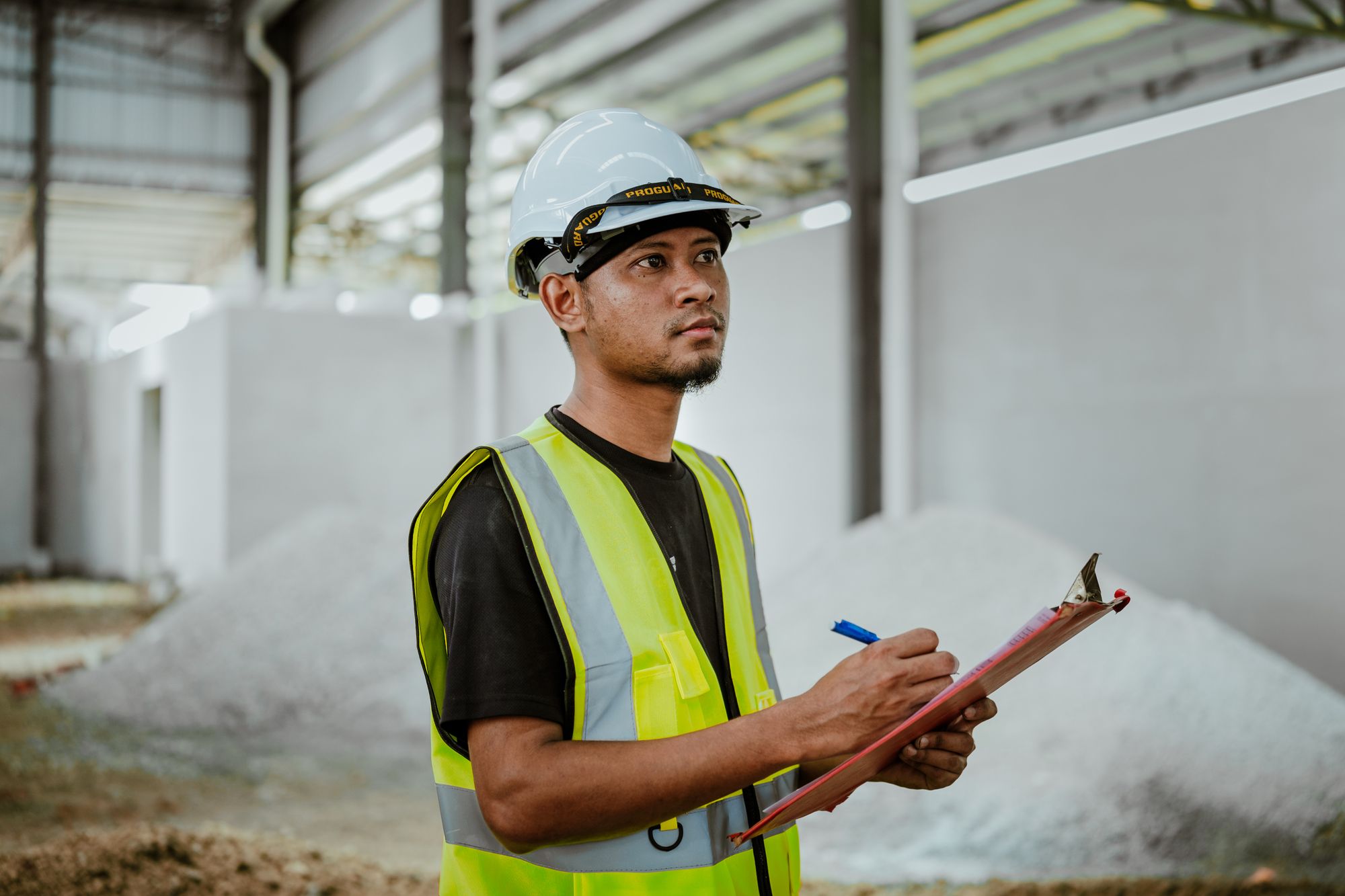 Safety inspector in a hard hat and high-visibility vest recording an inspection on a clipboard inside a building under construction