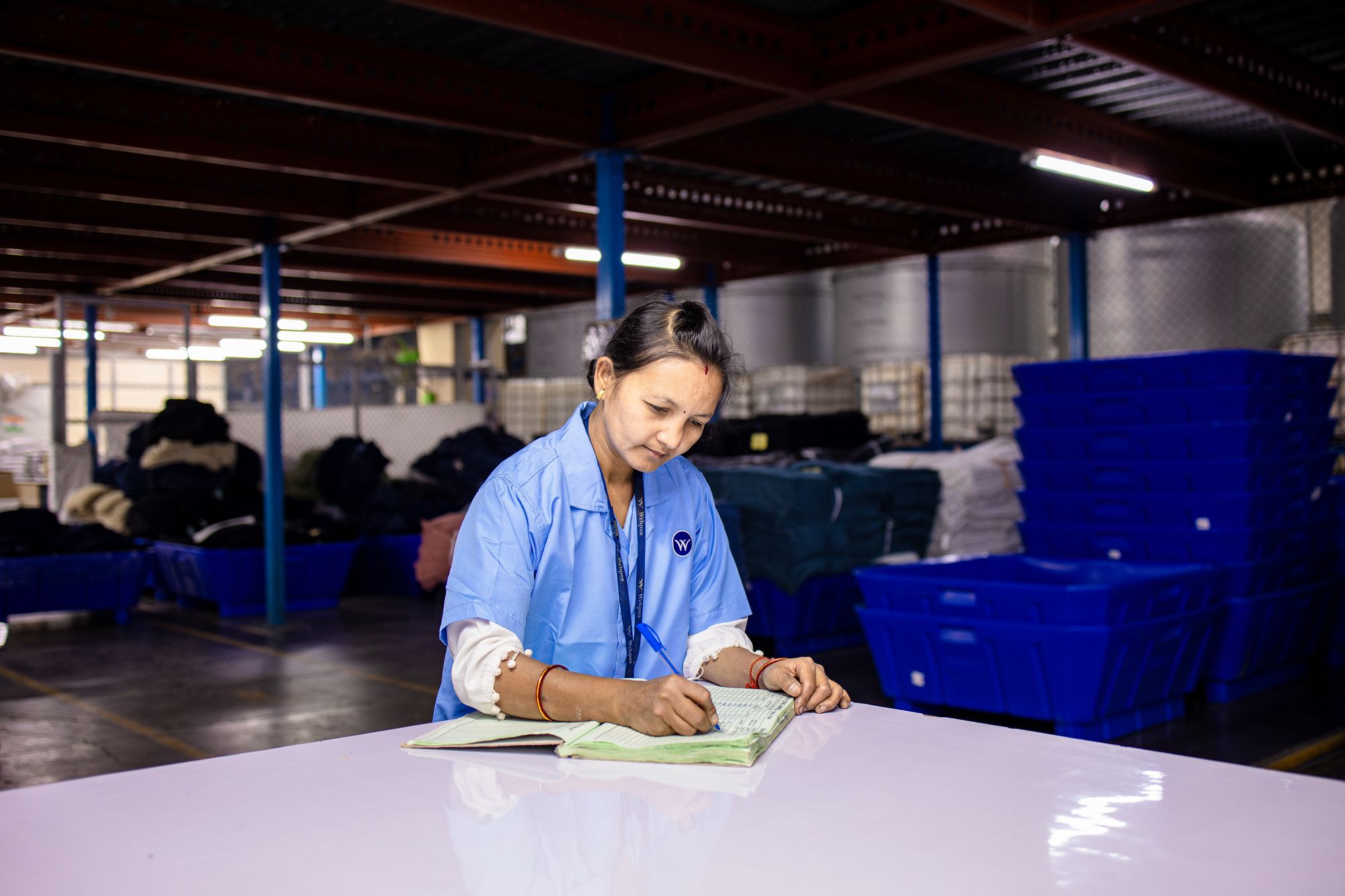 Warehouse worker writing entries in a paper logbook at a table