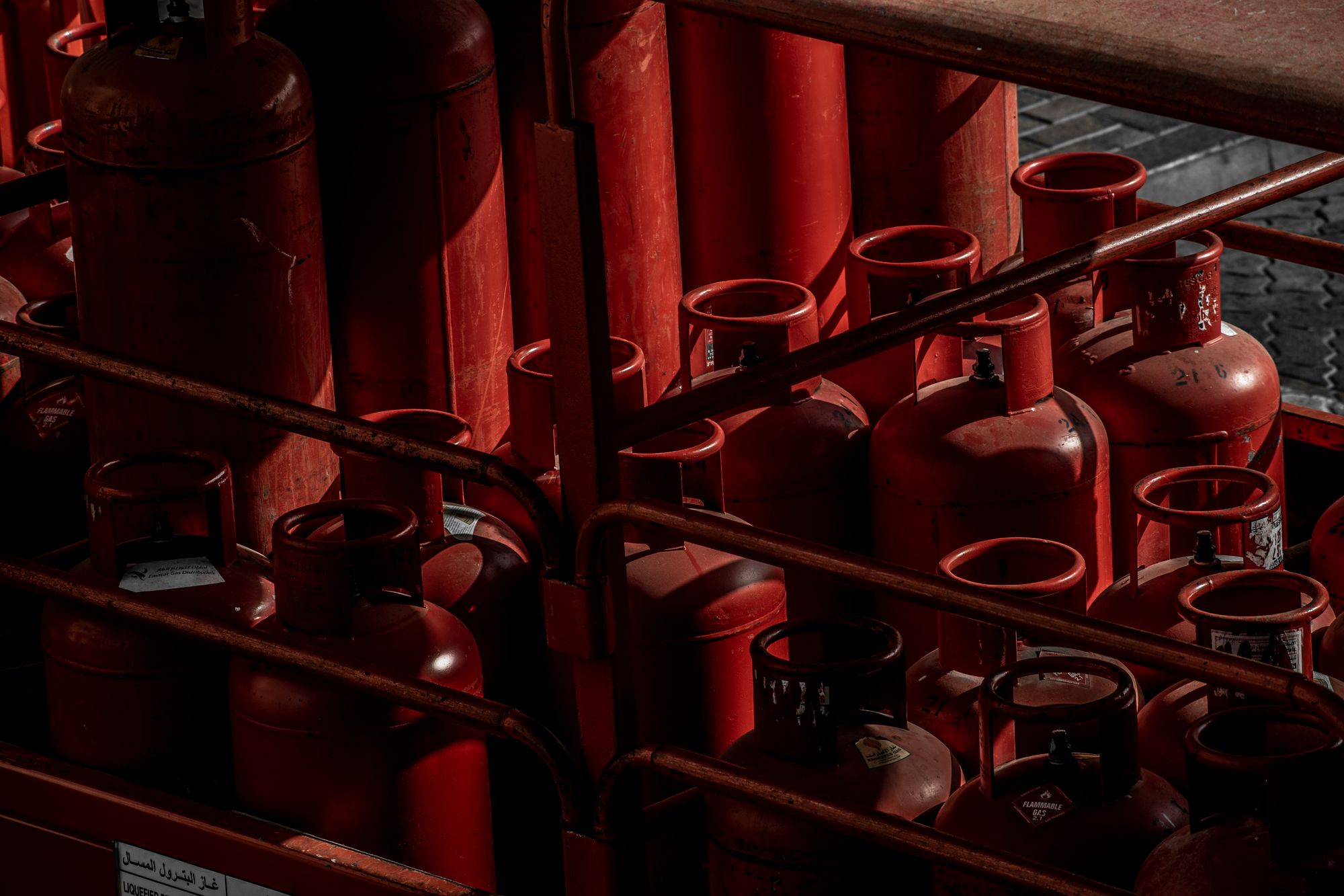 Rows of red compressed gas cylinders held upright behind the rails of a storage cage