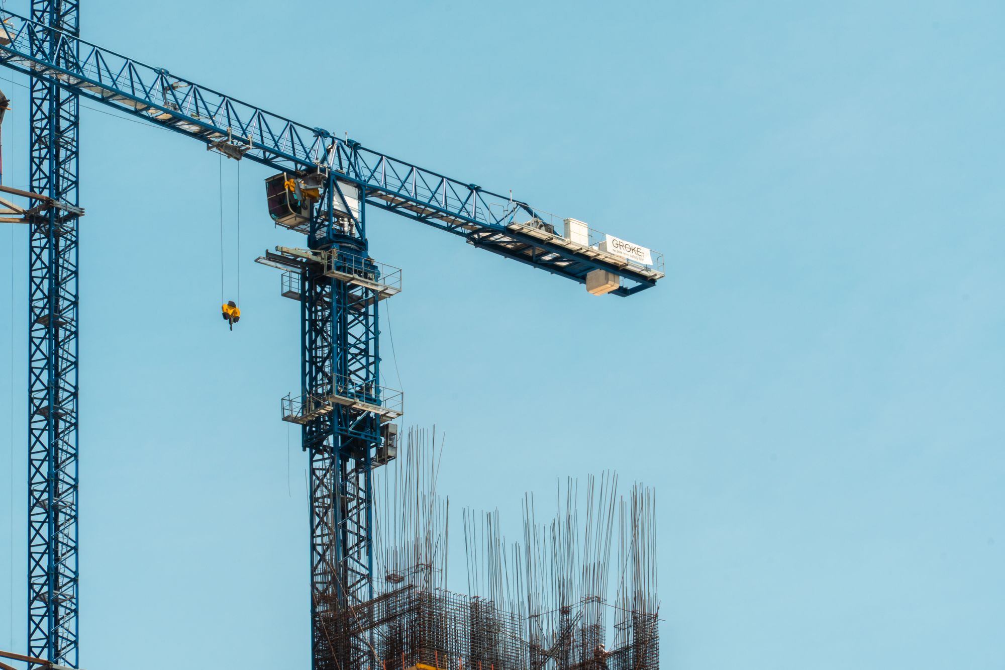 Tower crane jib with its hook lowered above vertical rebar cages on a building under construction