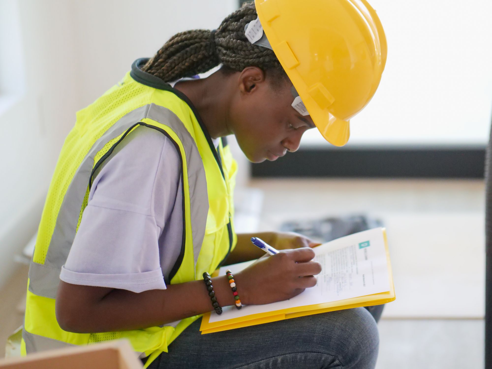 Worker in a hard hat and high-visibility vest filling out a paper form on a clipboard